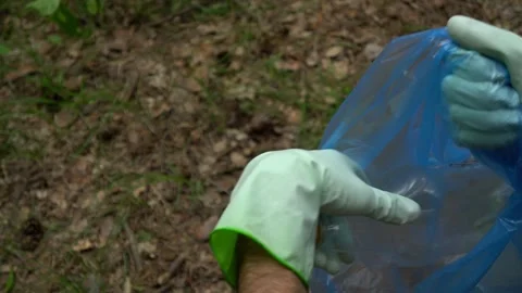 Hands of a young man in gloves throw a plastic bottle into a trash bag.  Stock Footage 132137158