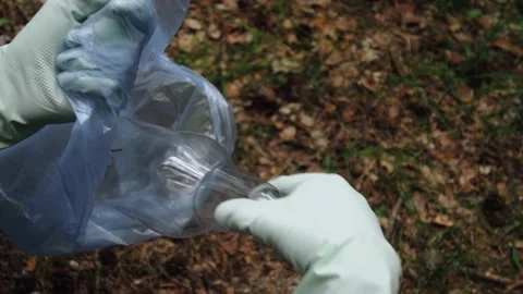 Hands of a young man in gloves throw a plastic bottle into a trash bag.  Stock Footage 132137198