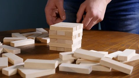 Hands of Young man plays jenga on blue background, close-up. A man builds a Stock Footage
