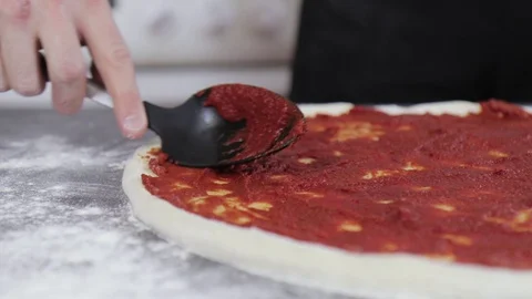 Hands of a young man put and smear tomato paste on pizza dough close up Video stock 127689638