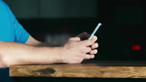 The hands of a young man sitting at a desk holding a mobile phone Stock Footage 310554720