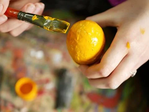 Hands of a young student, a brush with paint and a painted egg Stock Photos