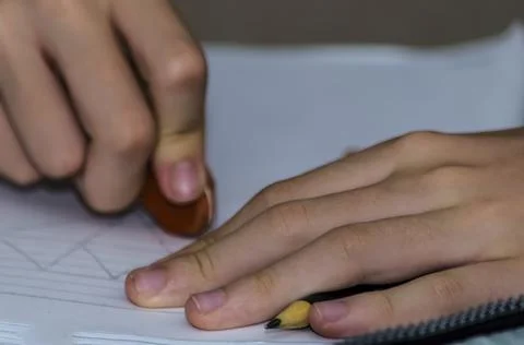 Hands of a young student erasing exercise done on school paper. Stock Photos