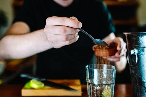 Hands of a young waiter, adding brown sugar in a large crystal glass to prepare Stock Photos
