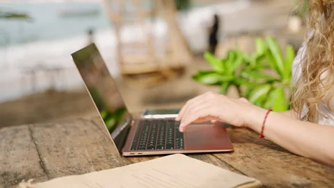 Hands of young woman coding on laptop in outdoor seaside cafe. Female freelancer Stock Footage 234539974