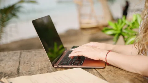 Hands of young woman coding on laptop in outdoor seaside cafe. Female freelancer Stock Footage 237429173