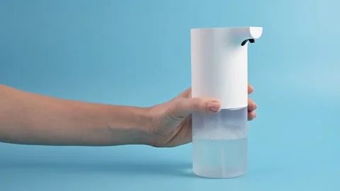 Hands of young woman picking up an automatic soap dispenser on blue background. 動画素材 170047844