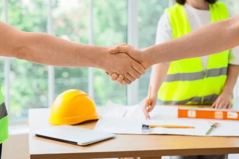 Handshake between construction workers over project plans Stock Photos