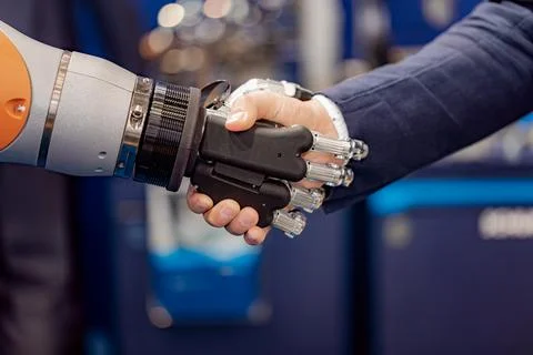 Handshake between human and robotic hand in business environment. Stock Photos