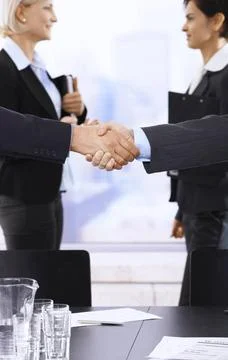 Handshake in focus Closeup handshake in focus, businesswomen smiling in ba... Stock Photos
