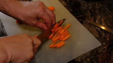 Handsof man in kitchen cutting carrot with knife Stock Photos