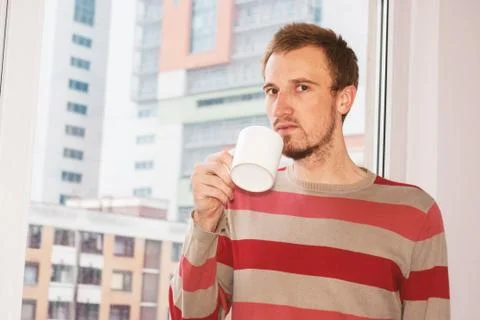 Handsom man standing by the window having coffee at home in the living room Stock Photos