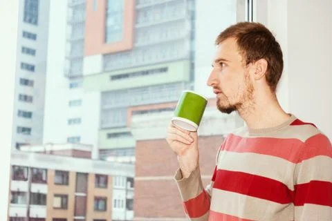 Handsom man standing by the window having coffee at home in the living room Stock Photos