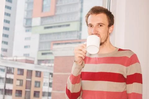 Handsom man standing by the window having coffee at home in the living room Stock Photos