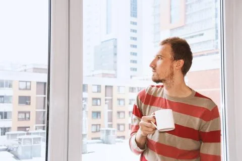 Handsom man standing by the window having coffee and looking on the citiy Stock Photos