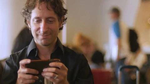 Handsome 30s man playing video game app on cell phone technology in airport Stock Footage