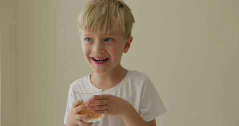 Handsome 5 year old boy drinks orange juice and licks lips 스톡 동영상 283047438