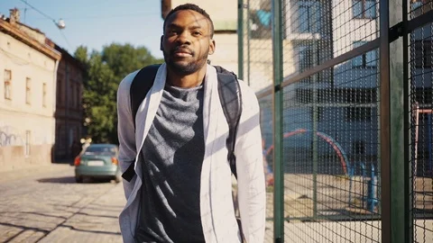 Handsome African guy with backpack on back holding black smartphone in hand Vidéo 92054151