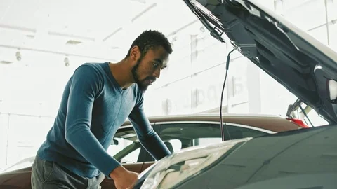 Handsome African man looking under the hood of a car at the dealership Stock-Footage 82183188