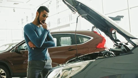 Handsome African man looking under the hood of a car at the dealership Stock Footage 82183684