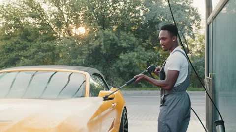 Handsome African young man in protective overalls, washing his yellow car Stock Footage 171657441