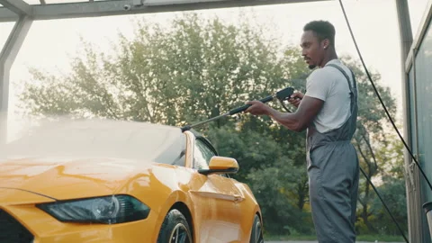 Handsome African young man in protective overalls, washing his yellow car Stock Footage 171657691