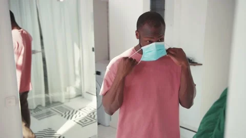 Handsome African young man putting on facial mask, getting dressed, wearing Stock Footage 131670367