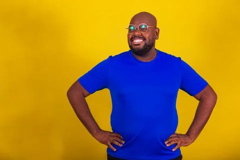 Handsome afro brazilian man wearing glasses, blue shirt on yellow background. Stock Photos