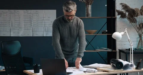 Handsome Aged Man standing at his Office room and looking at Large format Paper Stock Footage 126244306