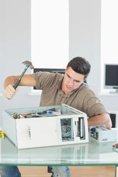 Handsome angry computer engineer destroying computer with hammer Stock Photos