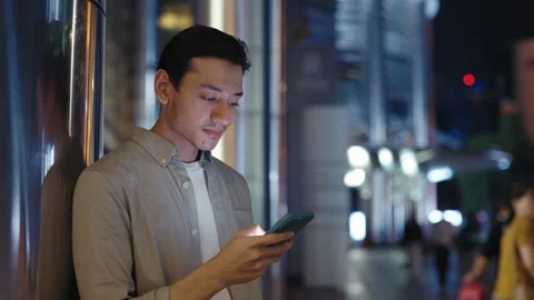 Handsome Asian Guy Scrolls Through the News Feed on a Smartphone While Standing Stock Footage 277189788