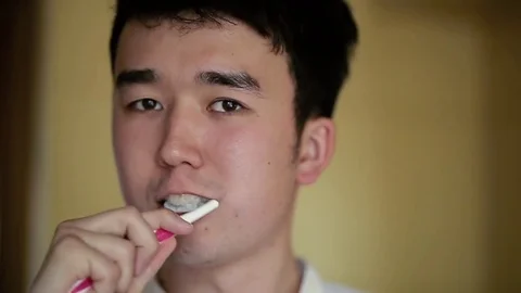 Handsome asian man brushing teeth and looking at the camera Stock Footage 76379813