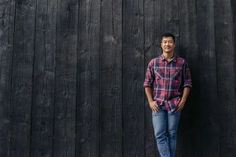 Handsome Asian man smiling while leaning against a wall outside Stock Photos