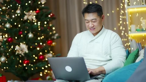 Handsome asian man uses laptop computer sitting at home on sofa during winter  Stock Footage 219912706