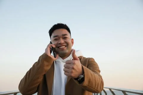 Handsome Asian man using and speaking on his smartphone on the beach. Freelance. 스톡 사진