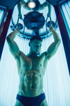 The handsome athletic man with beard on the face gets a tan in the sunroom. Stock Photos