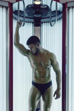 The handsome athletic man with beard on the face gets a tan in the sunroom. Stock Photos
