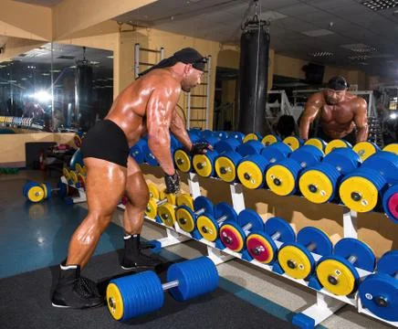 Handsome athletic man bodybuilder doing exercises with dumbbell in gym Stock Photos