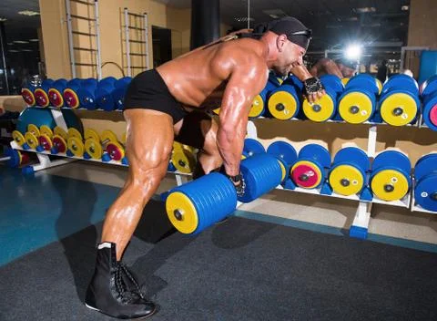 Handsome athletic man bodybuilder doing exercises with dumbbell in gym Stock Photos