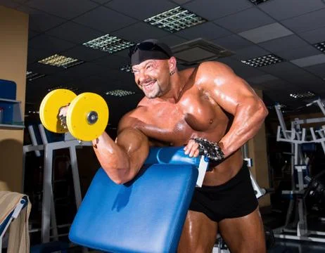 Handsome athletic man bodybuilder doing exercises with dumbbell in gym Stock Photos