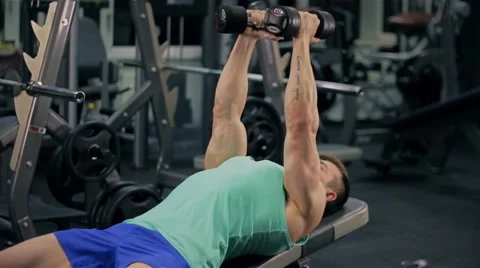 Handsome athletic man doing pectorals with breeding hands with dumbbells on benc Stock Footage 63220629