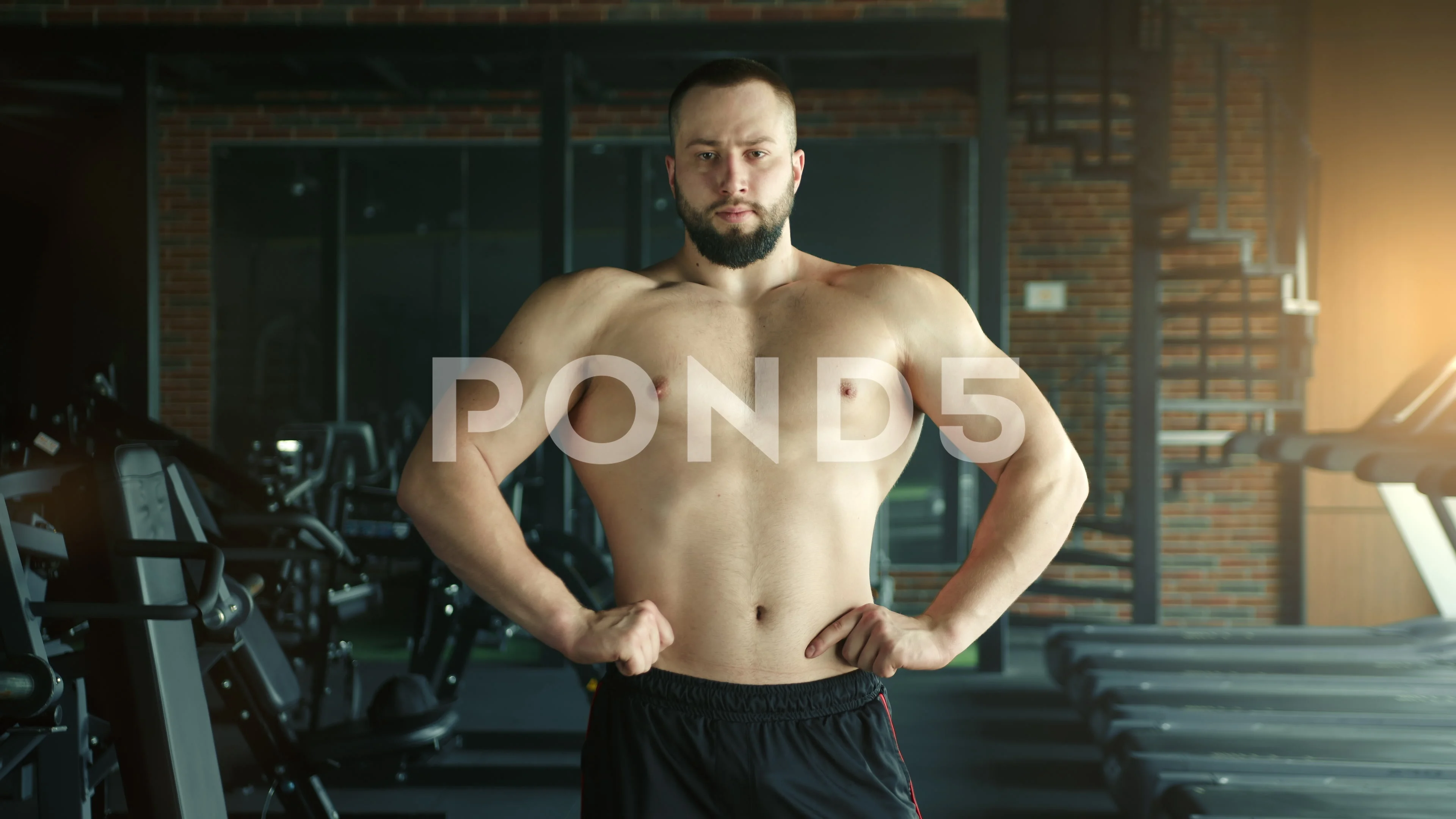 Handsome athletic young man with naked torso hands on waist standing in gym