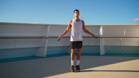 Handsome athletic young man in white t-shirt jumps on rope onboard cruise ship Stock-Footage 194440219