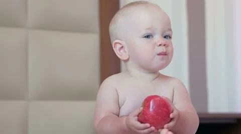 A handsome baby eats an apple in bed at breakfast. He bites off a piece and puts Stock Footage 67614876