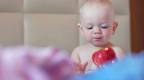 A handsome baby eats an apple in bed at breakfast. He bites off a piece and puts Stock Footage 67615067