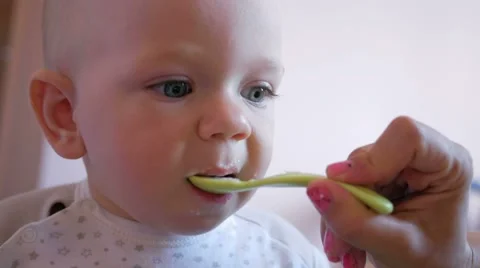 A handsome baby stares at one point and eating baby food with spoon. Tiny one Stock Footage 67621653