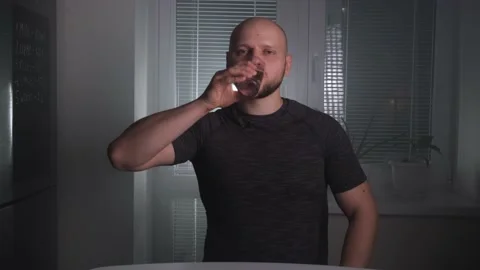 A handsome bald athletic man drinks clean water from a glass in the kitchen Stock Footage 168911242