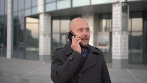 Handsome bald-headed man with beard talking on cellphone in the city. Blury Stock Footage 97117756