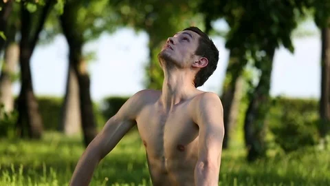 Handsome bare-chested man is meditating resting during yoga exercise in park Stock Footage 80372876