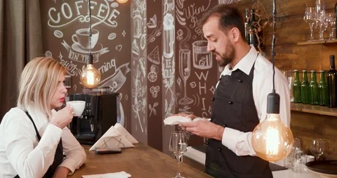 Handsome bartender in black apron talks with the waitress Video stock 104865323